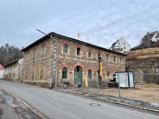 Alter, zweigeschossiger Steinbau mit roten Fensterrahmen an einer Straße.